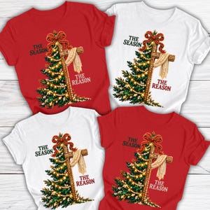 May include: Four short-sleeved t-shirts in red and white featuring a graphic of a Christmas tree merged with a wooden cross. The design includes a red bow, pearl-like strands, and the text THE SEASON THE REASON printed in black and red.