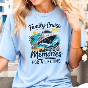 May include: A light blue t-shirt featuring a graphic of a cruise ship on ocean waves, a palm tree, a sun, and beach items. The text reads: Family Cruise 2027 Making Memories FOR A LIFETIME. The design includes a yellow sun and blue sunglasses.
