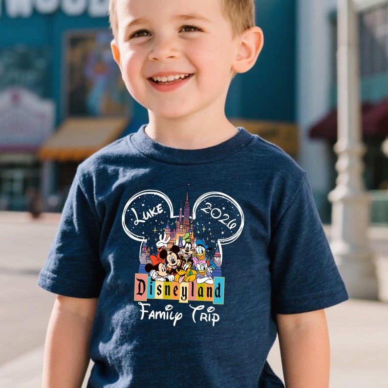 Puede incluir: Camiseta azul marino con un colorido dise&ntilde;o de Disneyland con Mickey Mouse, Minnie Mouse, Donald Duck y Goofy. La camiseta incluye el texto "Luke 2020" y "Disneyland Family Trip".