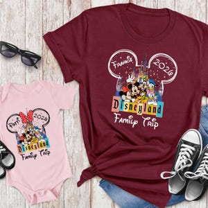 Puede incluir: Una camiseta granate y un body rosa con un dise&ntilde;o de "Disneyland Family Trip". El dise&ntilde;o incluye a Mickey y Minnie Mouse, el Pato Donald y Goofy. La camiseta tiene el nombre "Frankie" y el a&ntilde;o "2020" en un contorno de oreja de Mickey Mouse.