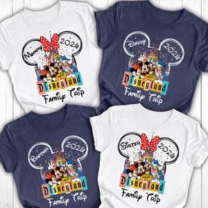 Puede incluir: Cuatro camisetas de manga corta con un dise&ntilde;o de Viaje Familiar a Disneyland. Cada camiseta presenta un contorno de la cabeza de Mickey Mouse con un castillo, personajes y el a&ntilde;o 2026. Las camisetas son blancas y azul marino, con texto para Mam&aacute;, Pap&aacute;, Hermano y Hermana.