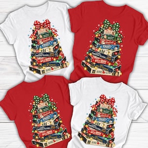 May include: Four short-sleeve t-shirts in white and red featuring a graphic of stacked VHS tapes arranged like a Christmas tree. The tapes are labeled with titles including Rudolph, Santa Clause, Frosty, Elf, Christmas Vacation, The Grinch, The Polar Express, and Home Alone, topped with a polka-dot bow and string lights.