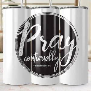May include: White tumbler with a black and white circular design. The design features the word "Pray" in a script font, with "continually" below it. The text "1 Thessalonians 5:17" is also included.