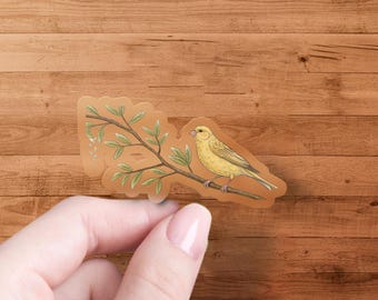 以下が含まれることがあります： 緑の葉のついた枝に止まっている黄色のカナリア。鳥は左を向いており、小さく尖ったくちばしをしています。