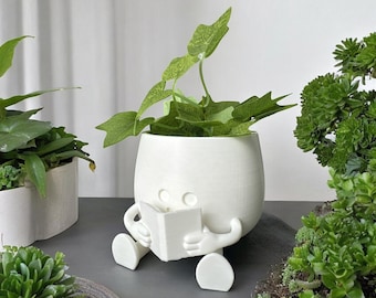 Maceta con forma de cara feliz, ideal como regalo para amantes de la lectura, ideal para decorar el hogar y la oficina, con un exclusivo soporte floral. Un solo color.