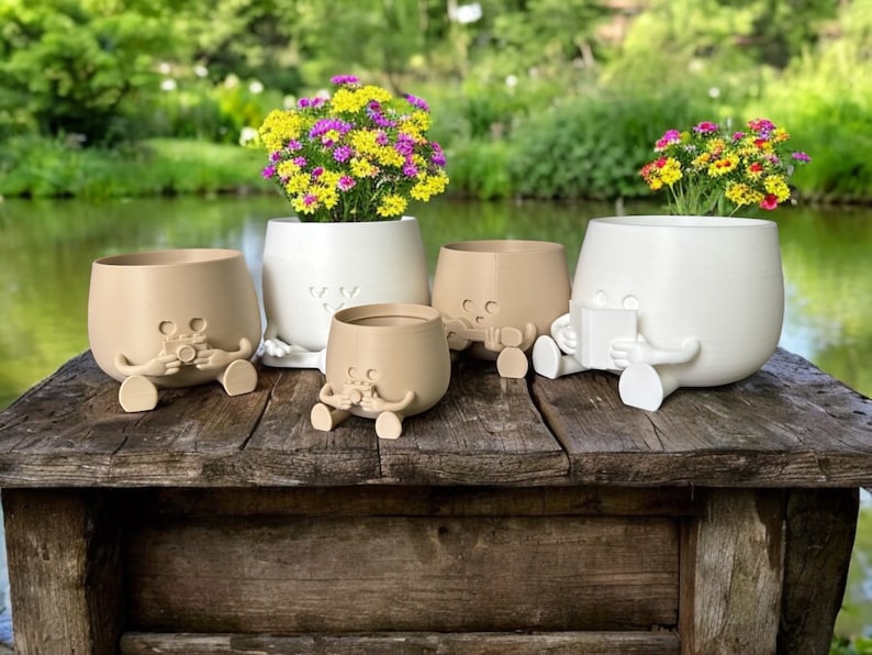 May include: Four ceramic planters with cartoon faces and legs. Two are brown and two are white. The planters are filled with flowers and are sitting on a wooden table.