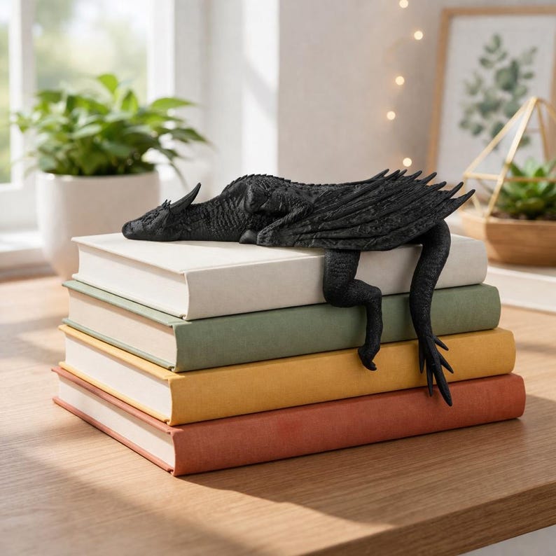 May include: A black dragon bookend rests on a stack of books. The dragon has detailed wings and a long tail that hangs down the side of the books. The books are in various colors, including white, green, yellow, and red.