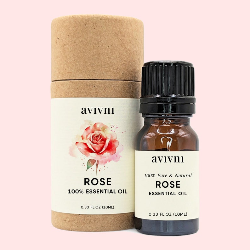 May include: A brown glass bottle and a cylindrical cardboard container of rose essential oil. The bottle has a black cap and a white label with the text "avivni", "100% Pure & Natural ROSE ESSENTIAL OIL", and "0.33 FL OZ (10ML)". The container has a watercolor rose illustration and the text "avivni", "ROSE 100% ESSENTIAL OIL", and "0.33 FL OZ (10ML)".