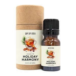 May include: A brown cardboard tube with a label that reads "avivnı Aromatic Oil HOLIDAY HARMONY 0.33 FL OZ (10ML)". The label features an illustration of a mug of spiced cider with a cinnamon stick, star anise, and orange slices. A small brown glass bottle with a black cap and a similar label is in front of the tube.