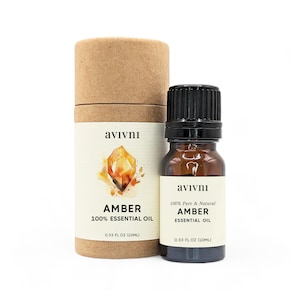 May include: A brown glass bottle with a black cap containing amber essential oil. The bottle is labelled "avivnı 100% Pure & Natural Amber Essential Oil 0.33 fl oz (10 ml)". The bottle is sitting on a brown cardboard tube with a label that says "avivnı Amber 100% Essential Oil 0.33 fl oz (10 ml)".