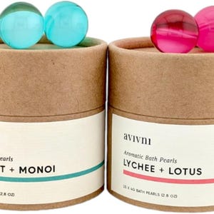 May include: Two cardboard tubes with lids, each containing bath pearls. The tube on the left has blue bath pearls and says "avivni Aromatic Bath Pearls COCONUT + MONOI 20 x 40 BATH PEARLS (2.8 OZ)". The tube on the right has pink bath pearls and says "avivni Aromatic Bath Pearls LYCHEE + LOTUS 15 x 40 BATH PEARLS (2.8 OZ)".