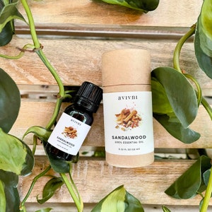 May include: Two bottles of sandalwood essential oil, one in a glass bottle and one in a cardboard tube. Both bottles have a white label with the text "avivni" and "Sandalwood 100% Essential Oil". The glass bottle is 0.33 fl oz (10 ml) and the cardboard tube is 0.33 fl oz (10 ml).