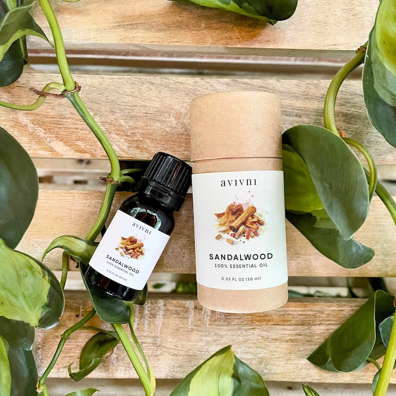 May include: Two bottles of sandalwood essential oil, one in a glass bottle and one in a cardboard tube. Both bottles have a white label with the text "avivni" and "Sandalwood 100% Essential Oil". The glass bottle is 0.33 fl oz (10 ml) and the cardboard tube is 0.33 fl oz (10 ml).