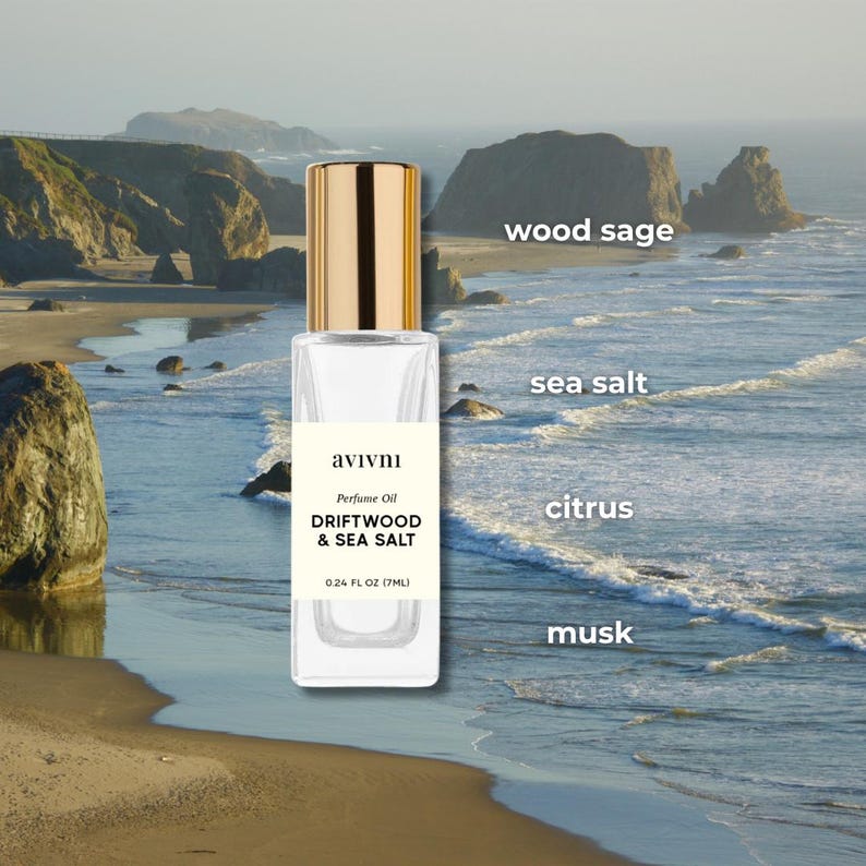 May include: A perfume oil bottle with a gold cap, labelled "DRIFTWOOD & SEA SALT" and "0.24 FL OZ (7ML)". The background shows a coastal scene with ocean waves and cliffs. The scent notes are wood sage, sea salt, citrus, and musk.