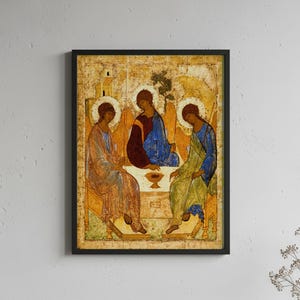 May include: A framed religious icon print depicting three figures with halos seated around a table. The central figure wears a dark red and blue robe, flanked by figures in blue and green garments. The background features gold tones and architectural elements.