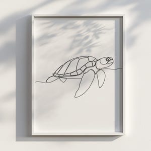 May include: A framed art print with a minimalist line drawing of a sea turtle. The black outline of the turtle is set against a white background, creating a modern aesthetic. The artwork is encased in a white frame, suitable for any room.