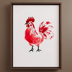 Puede incluir: Una lámina de arte enmarcada que presenta una ilustración estilizada de un gallo. El gallo está representado con pinceladas de color rojo vibrante sobre un fondo blanco. Tiene una cresta roja prominente, un pico negro y patas negras. El marco es de madera marrón oscura.