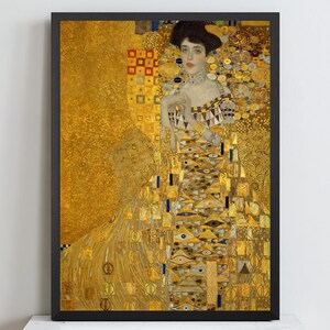 Puede incluir: Una impresión artística enmarcada del Retrato de Adele Bloch-Bauer I de Gustav Klimt. La pintura muestra a una persona con un vestido dorado adornado con patrones geométricos, triángulos y motivos de ojos sobre un fondo dorado brillante y texturizado.