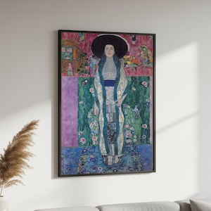 Puede incluir: Una impresión de arte mural rectangular enmarcada que muestra el retrato de una persona con un sombrero negro grande y una prenda larga estampada con detalles azules. El fondo presenta una composición abstracta vibrante y multicolor con secciones rosas, verdes y moradas.