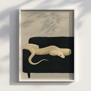 May include: A framed art print showing a detailed illustration of a pale snake on a black sofa. The snake's scales are finely detailed, set against a neutral beige backdrop. The print is enclosed within a white frame, adding a clean aesthetic.