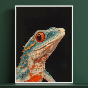 Op de afbeelding: Een ingelijste muurkunstprint met een gedetailleerde illustratie van een gekko tegen een effen zwarte achtergrond. De gekko heeft een levendige blauwe huid met oranje vlekken, een getextureerd schubachtig oppervlak en een groot, opvallend oranje oog.