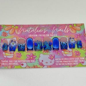 Puede incluir: U&ntilde;as postizas azules y blancas con dise&ntilde;o de estampado de leopardo, purpurina y pedrer&iacute;a. Las u&ntilde;as se muestran en una tarjeta con el texto "Natalie's Nails Custom Press On Nails" y la informaci&oacute;n de contacto.