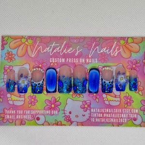 Puede incluir: Un conjunto de 10 u&ntilde;as postizas azules y blancas con una variedad de dise&ntilde;os, que incluyen purpurina, estampado de leopardo y flores. Las u&ntilde;as se muestran en una tarjeta rosa y blanca con el texto "Natalie's Nails Custom Press On Nails".