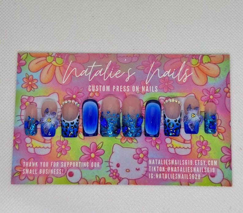 Puede incluir: Un conjunto de 10 u&ntilde;as postizas azules y blancas con una variedad de dise&ntilde;os, que incluyen purpurina, estampado de leopardo y flores. Las u&ntilde;as se muestran en una tarjeta rosa y blanca con el texto "Natalie's Nails Custom Press On Nails".
