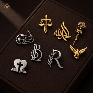 Puede incluir: Una colección de ocho pines metálicos en tonos oro y plata. Los diseños incluyen una espada y balanza, caligrafía árabe, una rosa con el nombre Smith, un balón de fútbol, las letras B y R, un pájaro, y un corazón con una cruz y un libro.