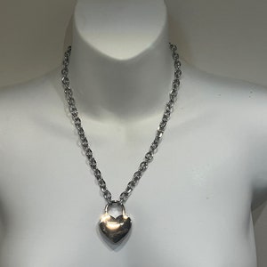 May include: A silver chain necklace with a heart-shaped padlock pendant.