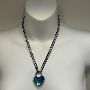 Può includere: Una collana a catena d'argento con un ciondolo a forma di lucchetto a forma di cuore. Il lucchetto è iridescente con sfumature di blu, verde e viola.