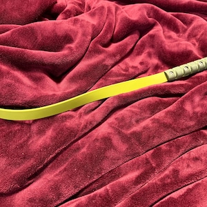 May include: A lime green, flexible, curved tool with a textured, olive green handle. The tool is lying on a deep red, plush blanket. The handle has a hole at the end.