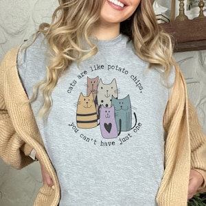 May include: Gray t-shirt with a graphic of cats and the text "Cats are like potato chips, you can't have just one."