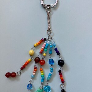 May include: A rainbow beaded keychain with a silver spring ring and a silver lobster clasp. The keychain features a variety of colourful beads, including red, orange, yellow, green, blue, and purple.