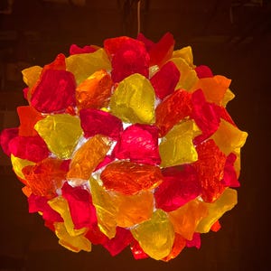 May include: A round pendant light fixture made of red, orange, and yellow glass pieces. The glass pieces are arranged in a cluster and are illuminated from within.