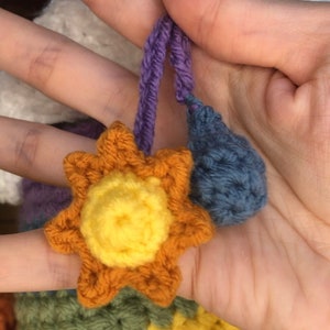 May include: A rainbow crocheted cloud with a yellow crocheted sun and a blue crocheted raindrop hanging from it.