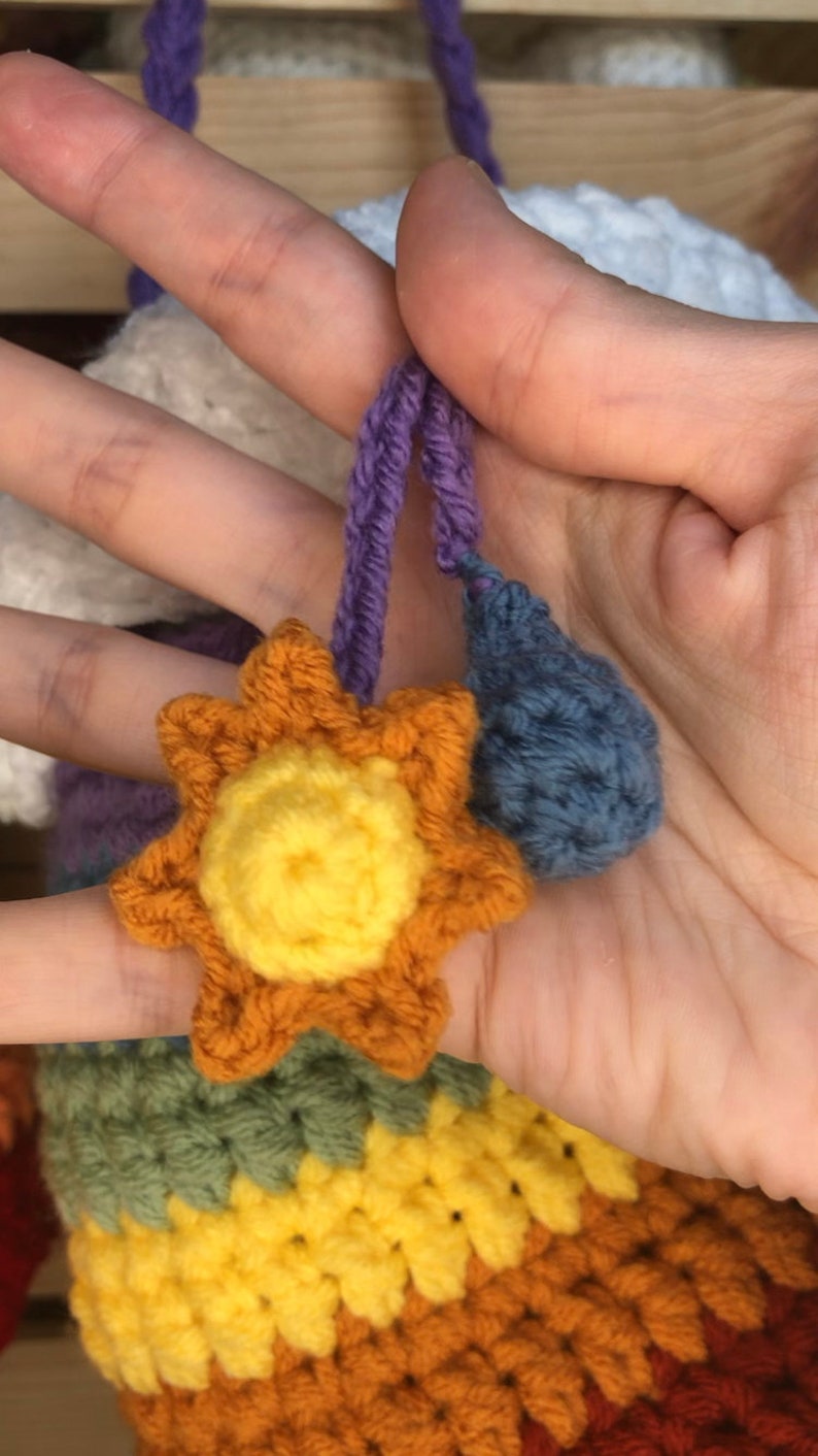 May include: A rainbow crocheted cloud with a yellow crocheted sun and a blue crocheted raindrop hanging from it.