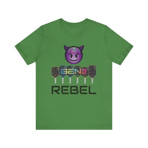 May include: Green t-shirt with a black and purple devil emoji, the text "GEN3" and "REBEL" in black, and a row of six colorful pickleball paddles.
