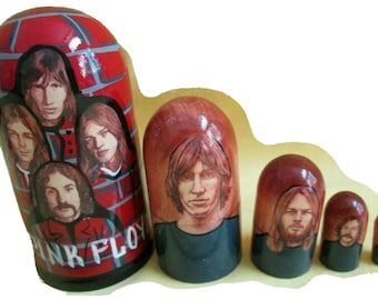 May include: Set of six nesting dolls, each painted with a different member of the rock band Pink Floyd. The largest doll is red with a brick pattern and features the band's name. The other dolls are painted in shades of red and blue.