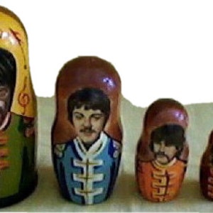 May include: Set of six nesting dolls, each depicting a different member of the Beatles. The largest doll is painted with a yellow background and features John Lennon playing a guitar. The other dolls are painted with brown backgrounds and feature Paul McCartney, George Harrison, Ringo Starr, and two smaller dolls.