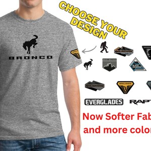 May include: A gray t-shirt with a black Ford Bronco logo. The shirt has a variety of different patches that can be chosen for customization. The patches include the words "Everglades" and "Raptor" and images of a Sasquatch, a mountain range, and a wave.
