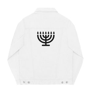 May include: White denim jacket featuring a black menorah graphic on the back. The jacket has a classic design with a button-down front, collar, and pockets. The menorah is a symbol of Judaism.