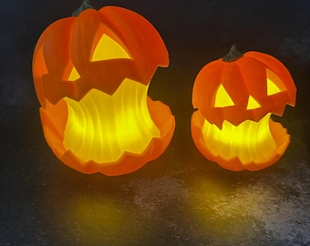 May include: Two orange Halloween jack-o'-lanterns with carved faces and glowing yellow interiors. The pumpkins have jagged edges around the mouths and triangular eyes. The background is dark.