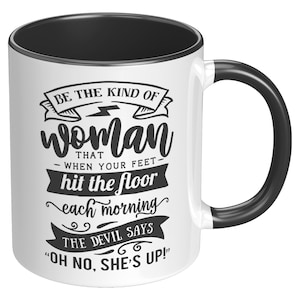 May include: White ceramic mug with a black interior, handle, and rim. The mug features the text "BE THE KIND OF woman THAT - WHEN YOUR FEET hit the floor each morning THE DEVIL SAYS 'OH NO, SHE'S UP!'" in black lettering.