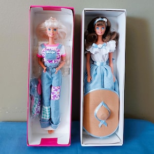 May include: Two Barbie dolls in their original boxes. One doll has blonde hair and wears denim overalls with floral patches and a white t-shirt. The other doll has brown hair and wears a blue gingham dress and a straw hat.