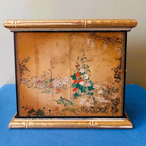 May include: A white ceramic mug with a black handle and the text "But First, Coffee" in a black, bold font. The mug is on a white surface.