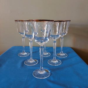 May include: Set of six clear glass wine glasses with a gold rim. The glasses are on a blue tablecloth.
