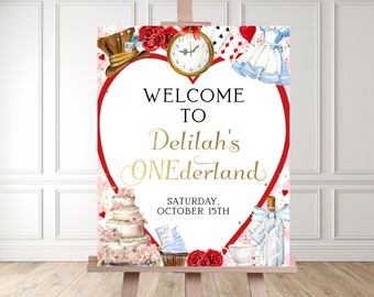 May include: A red heart-shaped welcome sign with gold lettering for a first birthday party. The sign says "Welcome to Delilah's Onederland" and includes a clock, playing cards, a teacup, a bottle, a cake, and a cupcake. The date of the party is Saturday, October 15th.