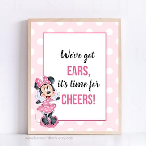 May include: A pink and white polka dot sign with a cartoon image of Minnie Mouse. The sign says "We've got ears, it's time for cheers!"