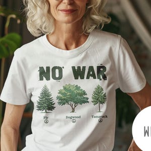 Puede incluir: Camiseta blanca con el texto "NO WAR" en verde y un gráfico de tres árboles: Abeto, Cornejo y Alerce. La camiseta también presenta símbolos de paz. Un círculo blanco con la palabra "WHITE" está en la esquina inferior derecha.